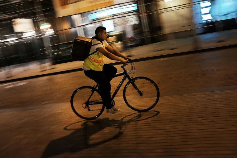 Entregador de bicicleta à noite em uma rua movimentada